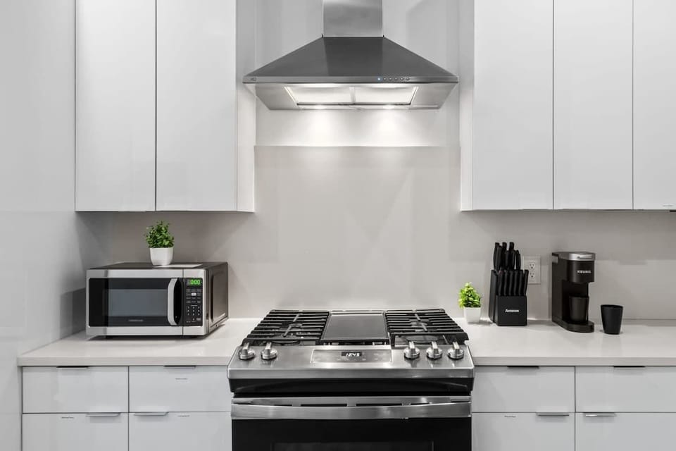This angle highlights the gas range, stainless steel hood, and microwave. Clean lines, bright lighting, and simple decor keep the space polished and guest-ready.