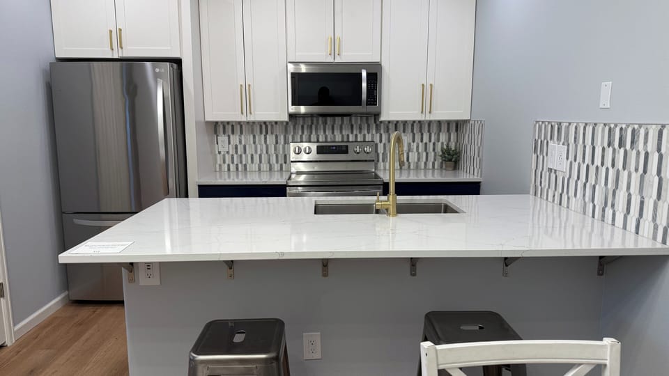 Your sleek, modern kitchen awaits with gleaming white countertops, stainless steel appliances, and a stylish geometric backsplash that catches the light beautifully.