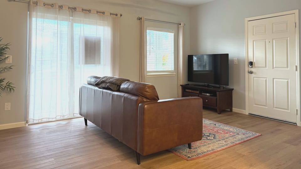 Relax in your bright, modern living space with plush leather seating and natural light streaming through sliding glass doors. The warm hardwood floors and cozy area rug create the perfect atmosphere for unwinding after your adventures.