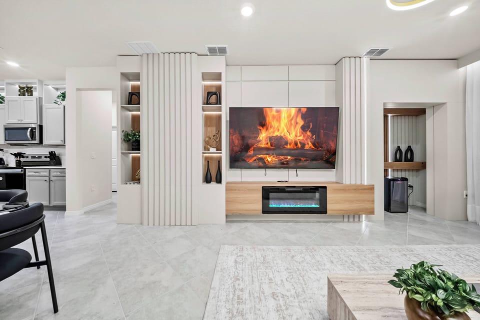 Enter a bright living area with sleek, light cabinetry and a modern entertainment setup, featuring a cozy digital fireplace. The soft textures of the furniture and open layout create a perfect space for relaxation and connection.
