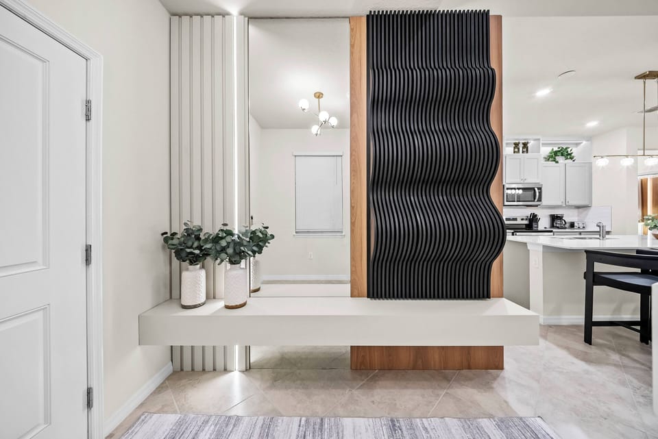 Welcome to a beautifully designed entryway with a striking wave-patterned wall that adds character. Soft natural light fills the space, complemented by stylish planters that introduce a refreshing touch of greenery.