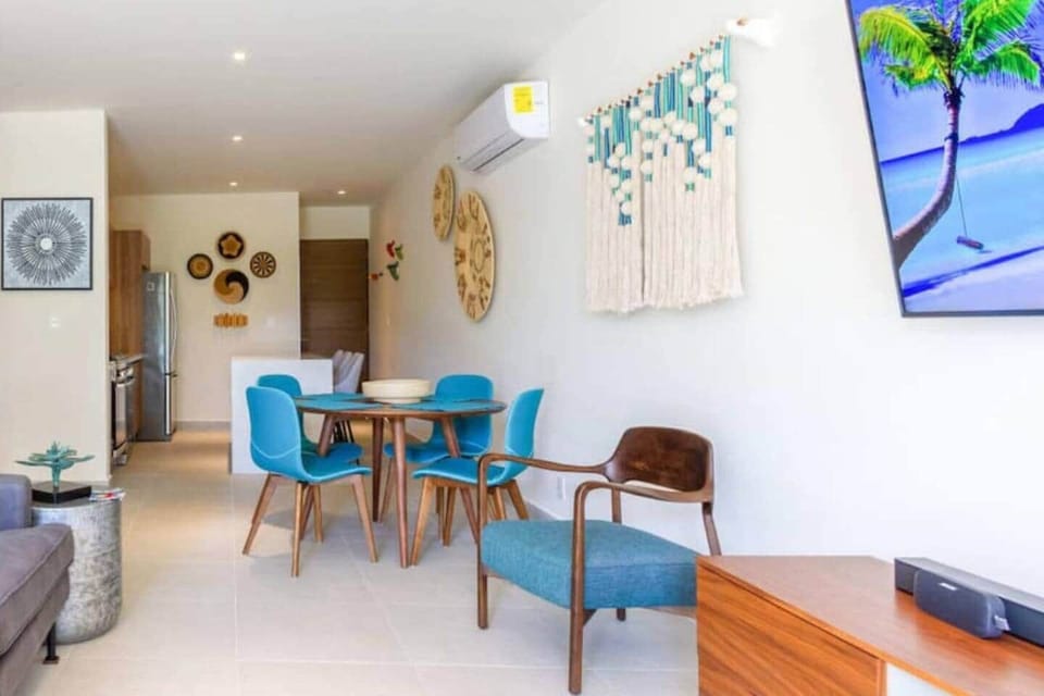 Bright and stylish dining area with seating for four, featuring vibrant accents and a warm, inviting atmosphere. The open layout flows into the kitchen and living room, with air conditioning for added comfort.