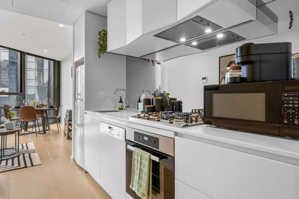 Fully equipped white kitchen with gas cooktop, oven, dishwasher, microwave, and Nespresso machine, flowing directly into the dining area and balcony beyond. A well-designed layout that makes cooking and entertaining easy.