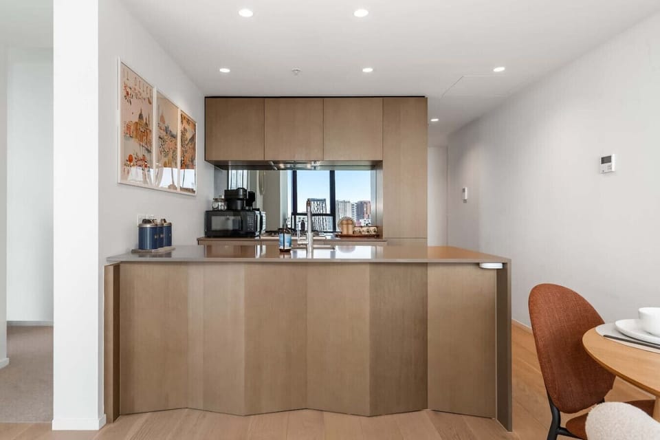 Open kitchen with a curved timber island, mirrored splashback reflecting the city skyline, and a cozy dining nook just steps away - a stylish spot to cook, gather, and take in the view.