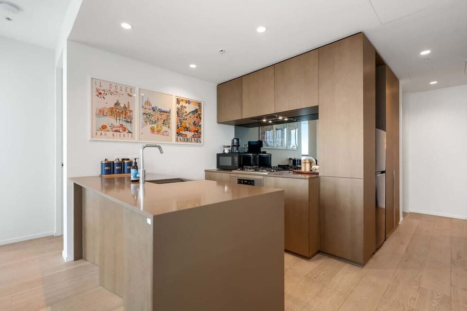 Modern kitchen with a spacious island, warm timber cabinetry, and light wood floors, styled with playful Italian-inspired art - a bright, open space that feels both stylish and easy to move around in.
