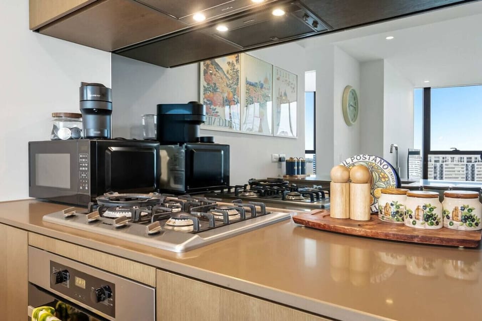 Sleek gas cooktop kitchen with an espresso machine, oven, and skyline views through floor to ceiling windows - a fully equipped space for guests who love to cook and unwind with a view.