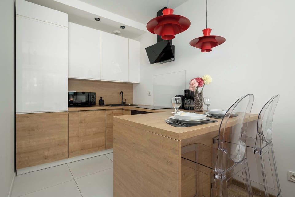 Compact kitchen area with wooden cabinets, white backsplash, and red pendant lights.