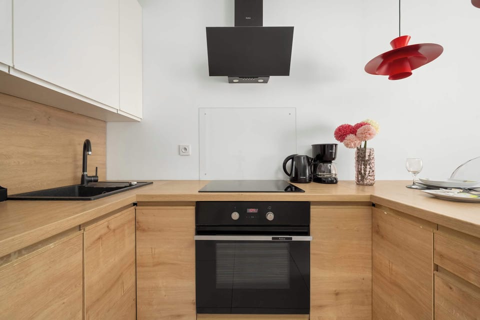 Compact kitchen area with wooden cabinets, white backsplash, and red pendant lights.