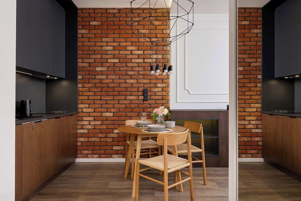 The brick wall and black kitchen accents add a modern touch, while the wooden table invites shared meals.