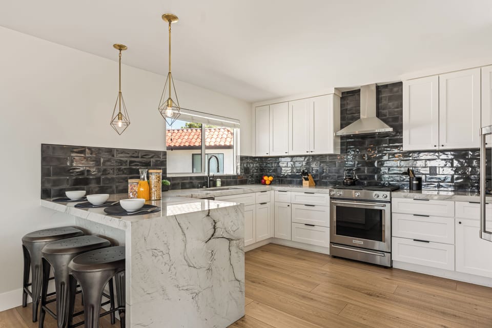Sleek modern kitchen with marble waterfall island, stainless steel appliances, and chic black tile backsplash—perfect for gathering and entertaining. (Unit 1)