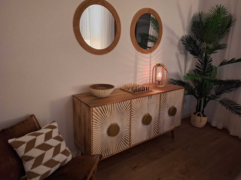 Stylish corner with a sunburst sideboard, chessboard, warm lantern light, and earthy textures—framed by mirrors, a cozy chair, and lush greenery, creating a relaxed nook perfect for quiet games or thoughtful moments.