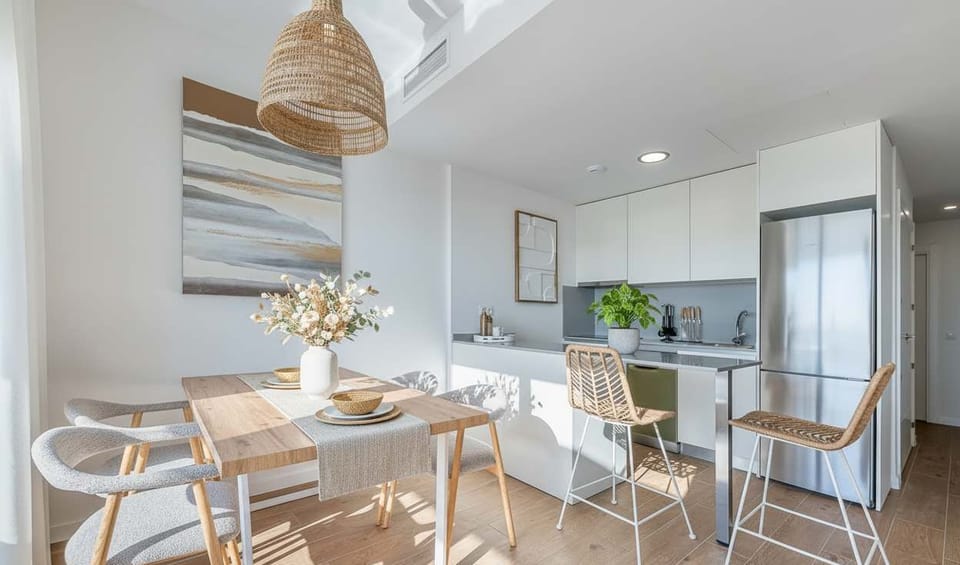 Minimalist kitchen-dining with wood table, woven pendant, white cabinetry, and wicker stools. Bright, airy design blends natural textures with modern comfort.