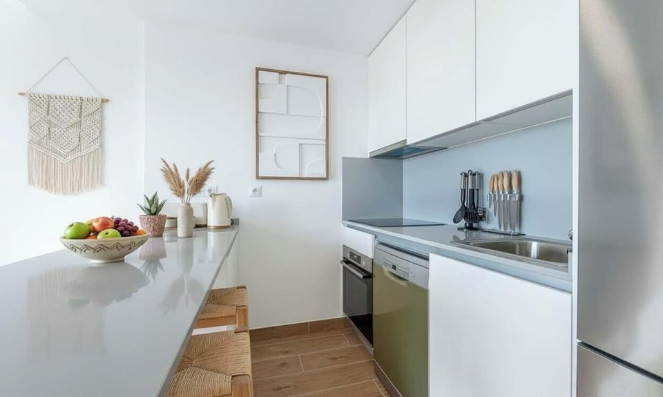Minimalist kitchen with white cabinetry, gray counters, wood floors, and light blue backsplash. Warm accents and sleek design create a stylish, functional space.