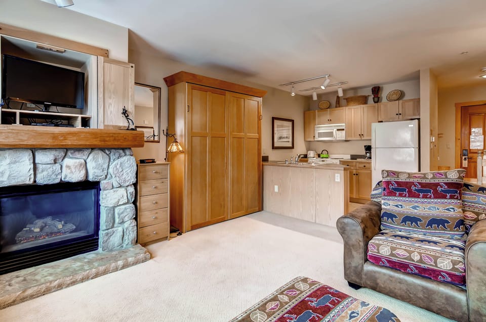 Cozy studio corner with a stone fireplace and wooden accents creating a warm mountain retreat atmosphere.