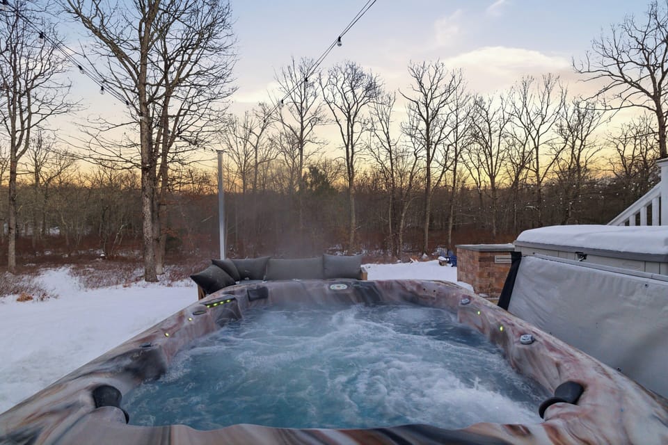 Relaxing outdoor hot tub surrounded by snowy woods at sunset.