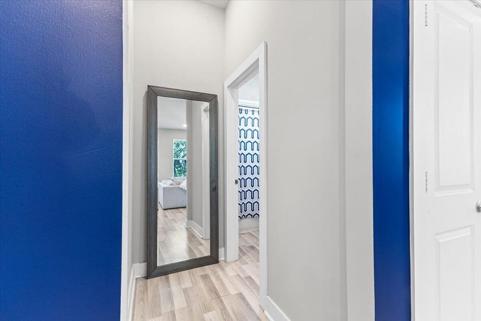 Bright hallway with light wood floors, bold navy accents, and a full-length mirror leading to stylish bedrooms.