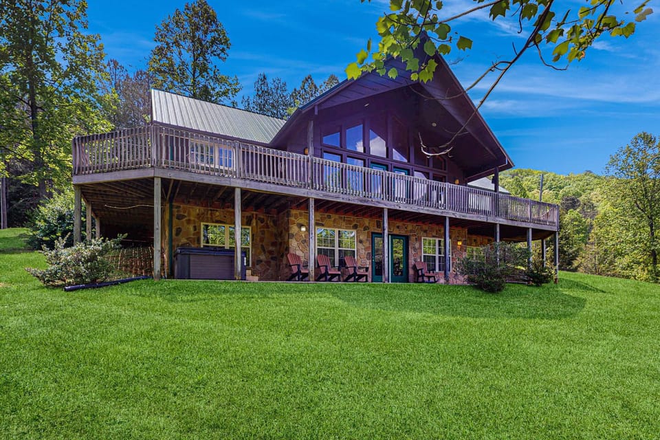 Spacious Smoky Mountain cabin with wraparound deck, stone exterior, and large grassy yard. 