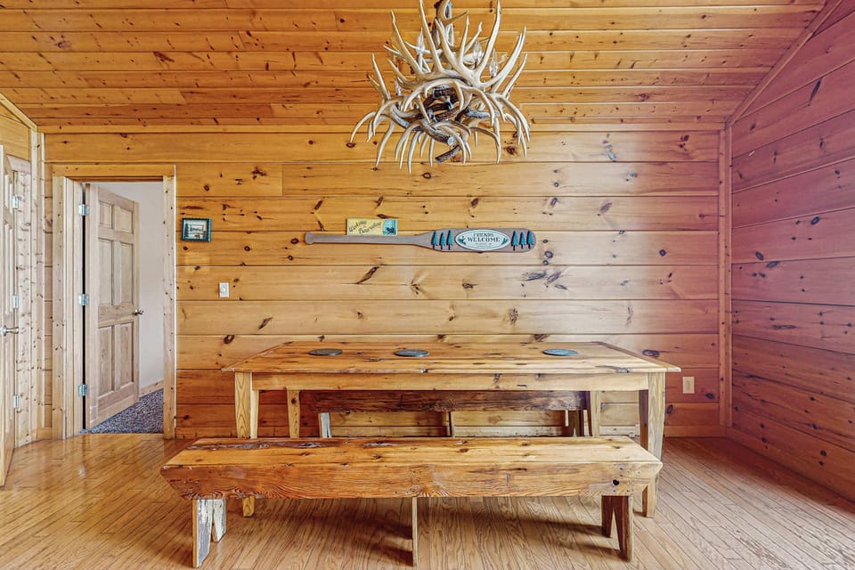 Rustic cabin dining room with handcrafted table, bench seating, and antler chandelier. 