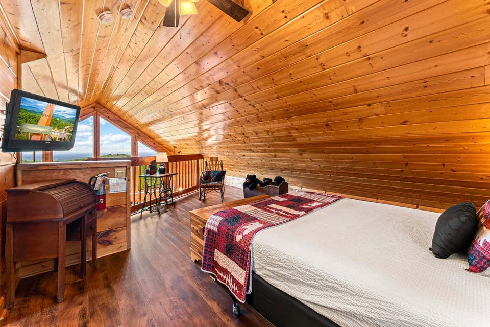 Cozy loft bedroom with vaulted wood ceilings, comfortable bed, TV, and peaceful mountain views.