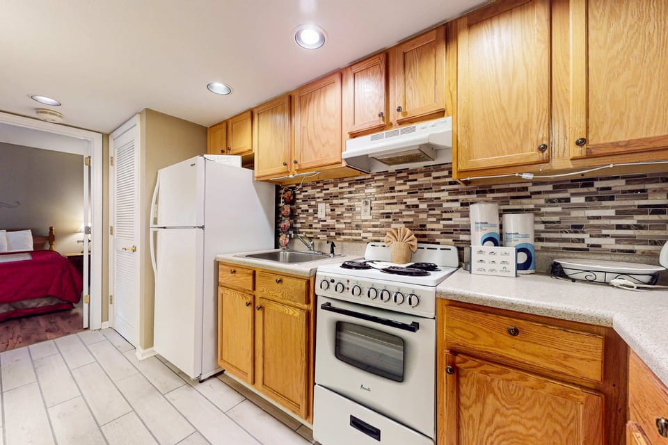 Bright galley kitchen with full-size fridge, stove, and counter space. Ideal stay for cooking and longer stays; stocked essentials, clean tile floors, and easy access to bedroom for convenient vacation living.