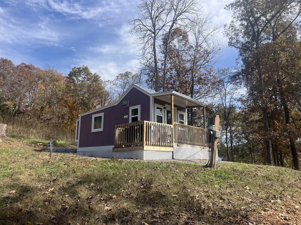 Side view of the tiny cabin with wraparound deck on a hillside. 
