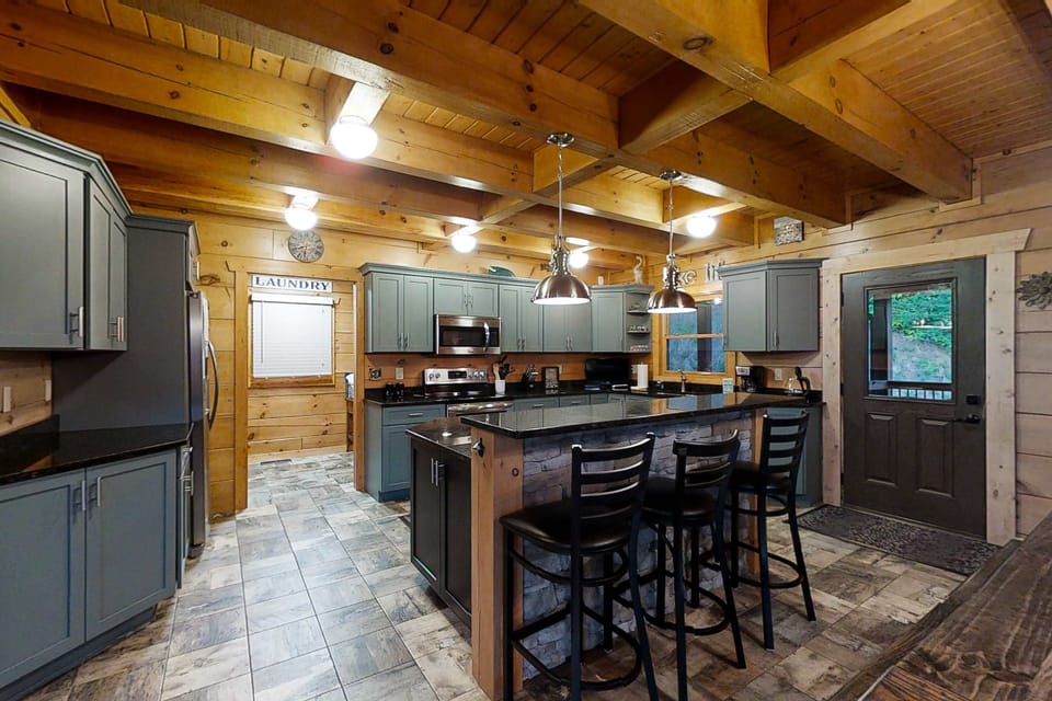 Rustic log cabin kitchen with granite island, bar seating & stainless appliances. Perfect for family meals. Open-concept, modern farmhouse style, cozy wood beams. Ideal Smoky Mountain Cabin getaway.