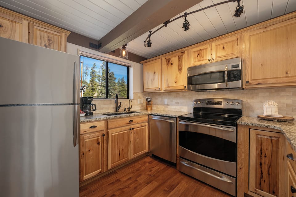 Your rustic mountain kitchen features warm wood cabinets and granite counters, perfect for preparing meals while enjoying forest views.
