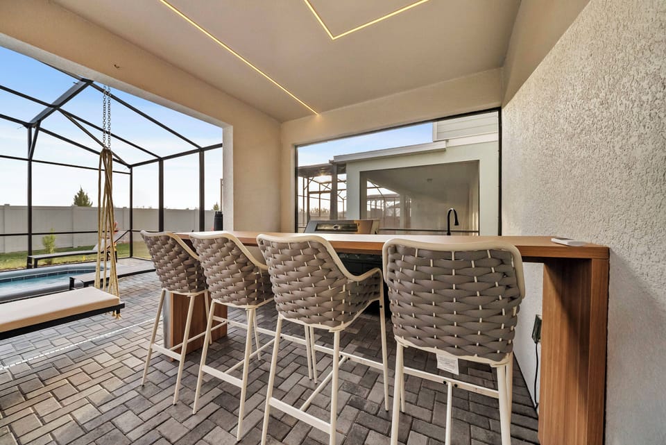 Enjoy the natural light while you relax at the sleek wooden bar with stylish rattan stools, ideal for casual meals or evening drinks, all complemented by expansive glass views that connect you to the inviting outdoor space.