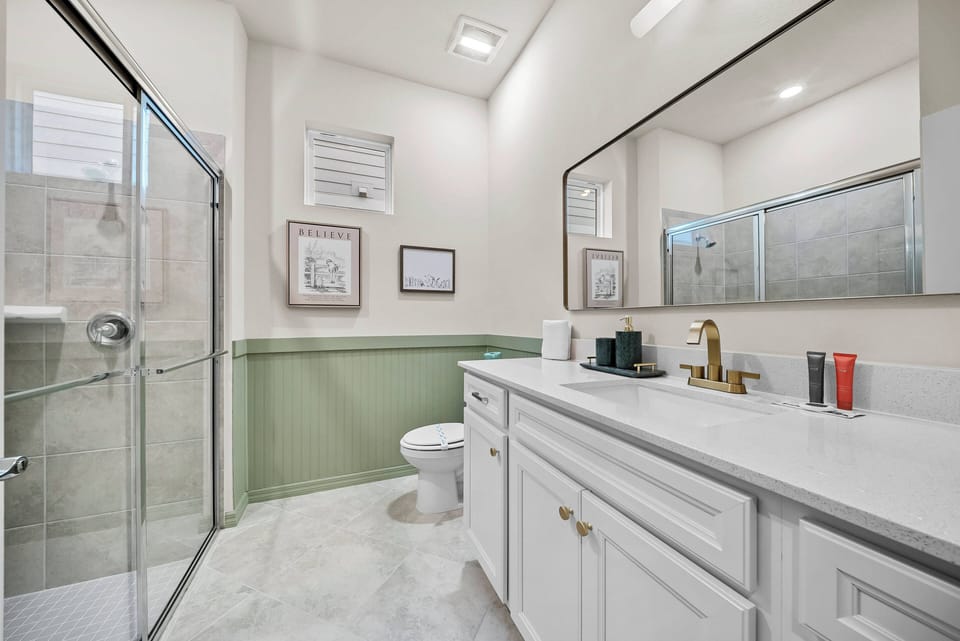 This bright, airy bathroom boasts a spacious walk-in shower with glass doors and a chic white vanity with elegant fixtures. Soft green accents add a refreshing touch, creating the perfect space to unwind after your adventures.