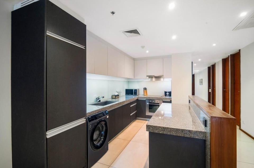 Fully equipped modern kitchen with granite countertops, built-in appliances, washing machine, and ample storage space.