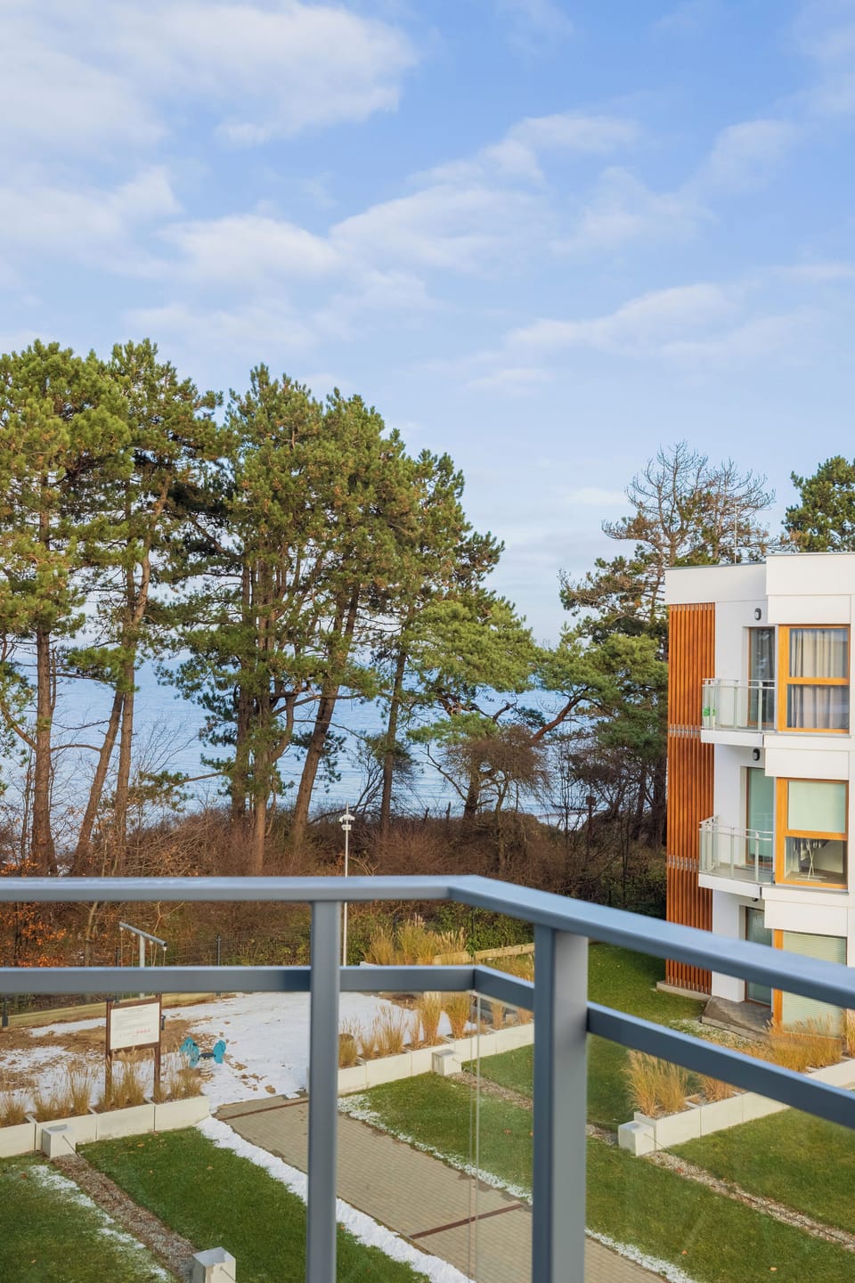 An outdoor view of modern apartment buildings surrounded by trees. A landscaped garden sits between the structures. The area appears peaceful and well-maintained.