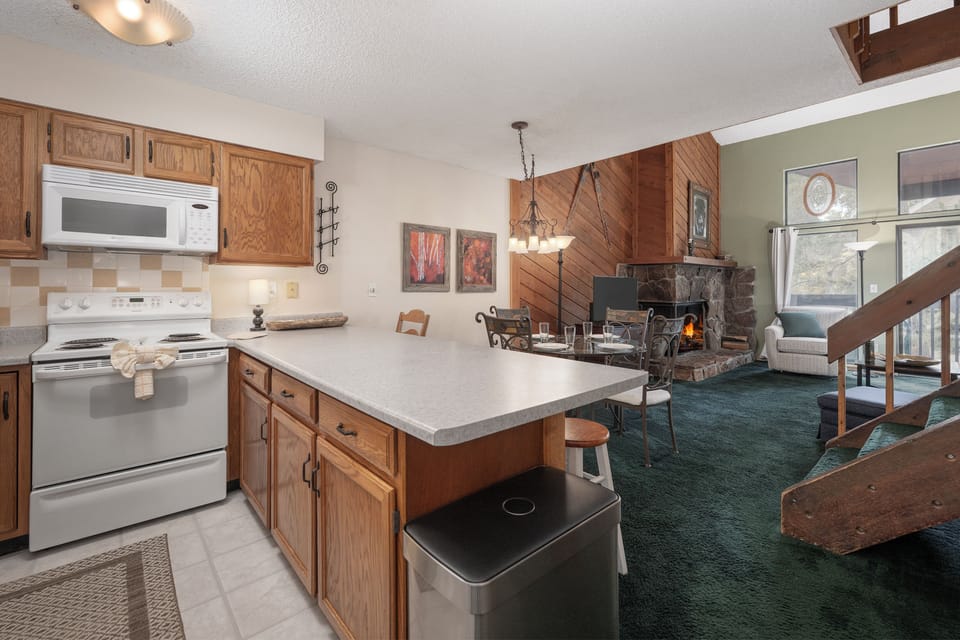 Your cozy mountain retreat features a fully equipped kitchen flowing into a warm living space with crackling stone fireplace.