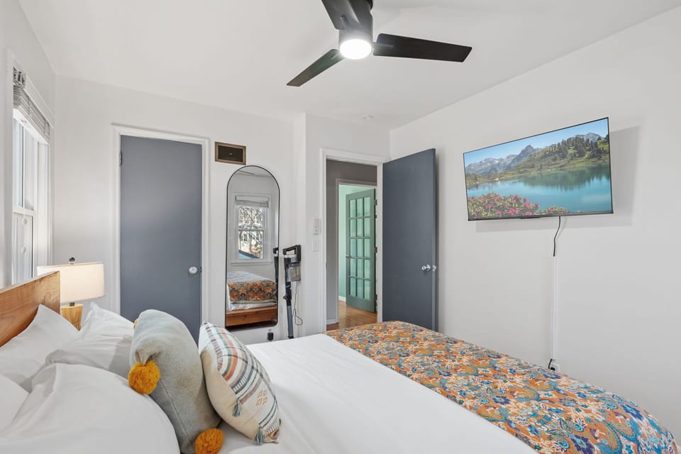 Drift off peacefully in your bright bedroom with cozy linens, ceiling fan, and large screen for evening relaxation.