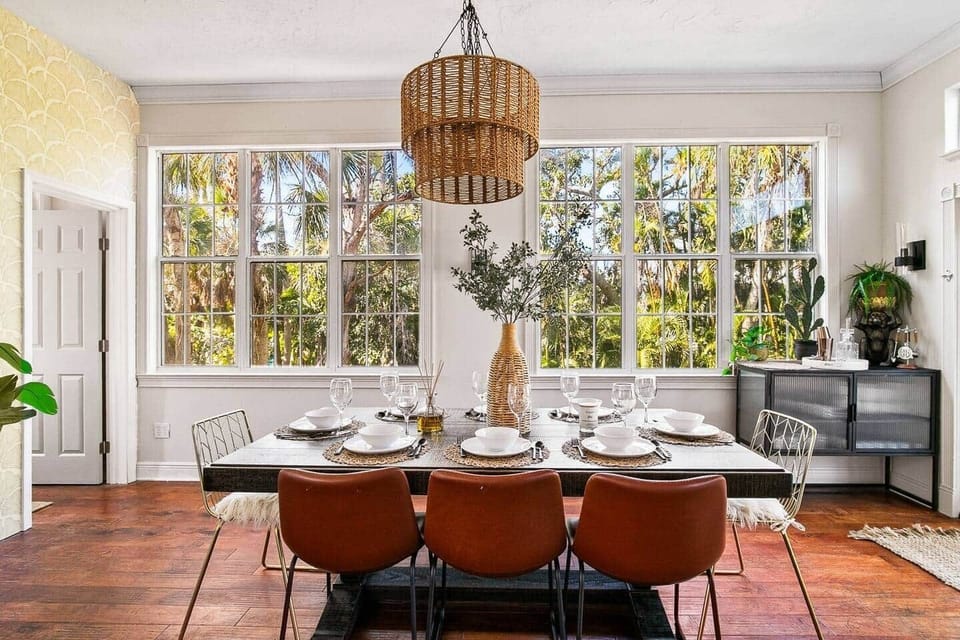 Open-concept dining with farmhouse table, wicker chandelier, French doors to deck, and seamless flow into the chef's kitchen.