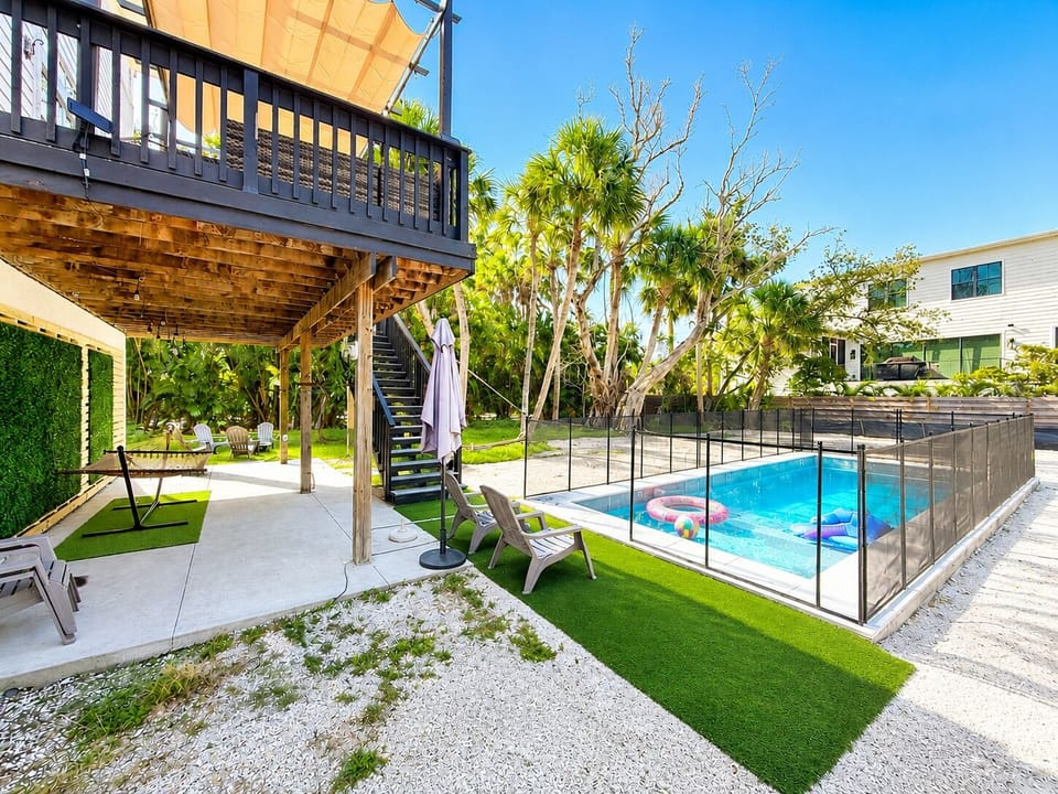 Private pool with safety fence, lounge chairs, artificial turf, hammock area, and covered lower patio beneath the elevated deck.