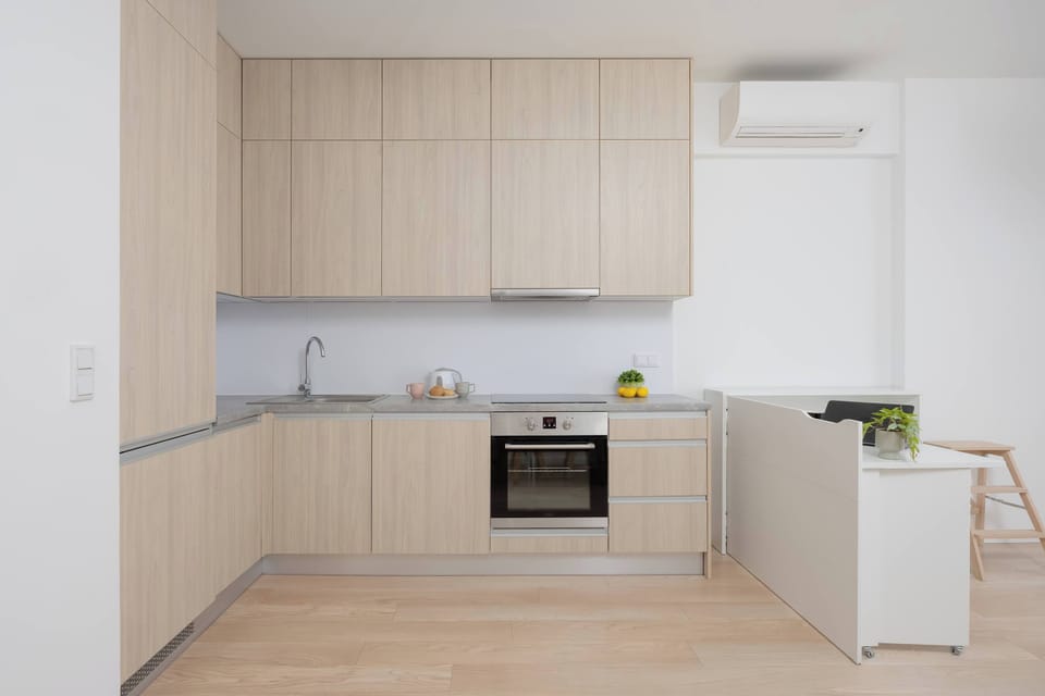 The kitchenette in a modern open-plan layout with light wood cabinets. Appliances include an oven, induction cooktop, and refrigerator.