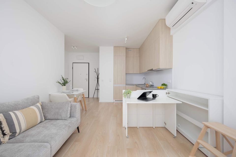 Another view of the living area showing the sofa, kitchenette, and dining space. The room feels open and airy with minimalist decor.