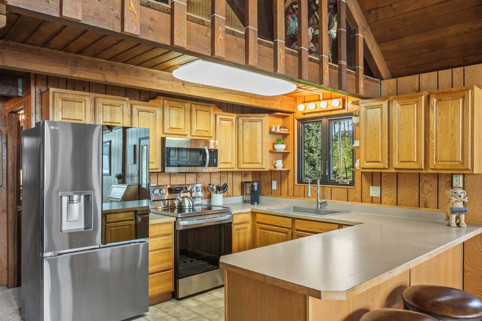 Full kitchen with peninsula bar seating, stainless appliances, and soaring A-frame loft above — plenty of room to fuel the whole crew