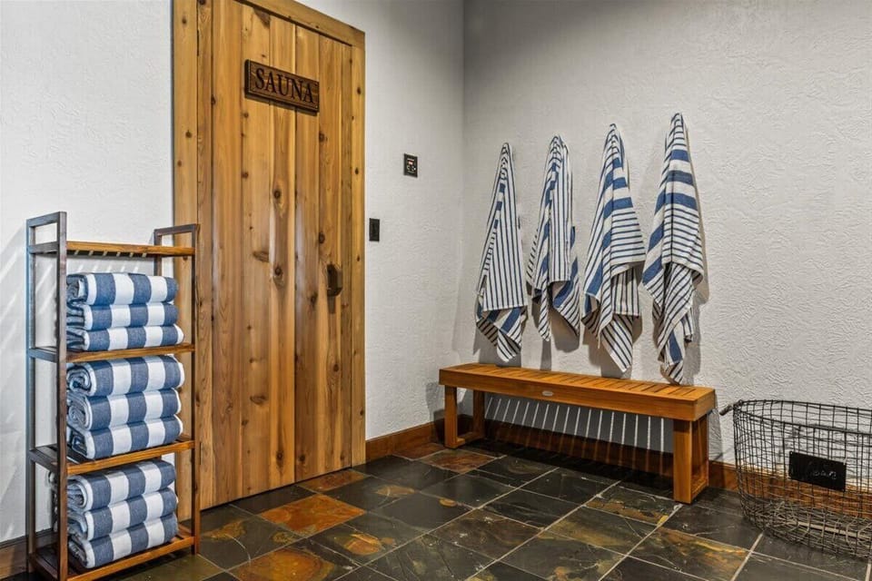 Sauna with cedar door, stacked towel rack, teak bench, and wall hooks — everything ready before you step into the heat