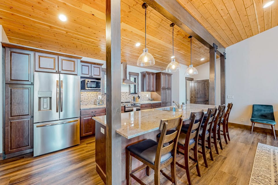 An open-concept kitchen featuring large countertops, a spacious breakfast bar with seating, warm wood finishes, and modern appliances.