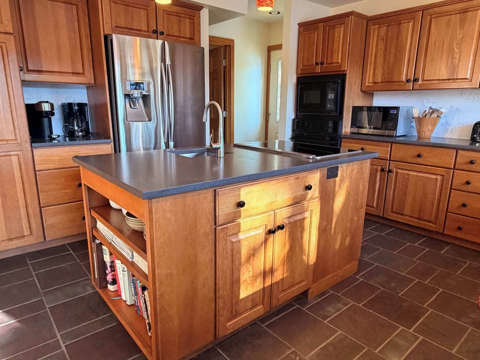 Full kitchen with center island sink, dark counters, stainless fridge, and wall oven — stocked so no one needs to eat out