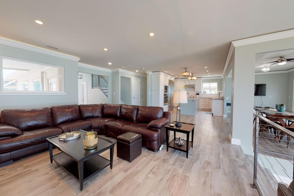 Bright, open-concept living room perfect for your beach stay. Features a large leather sectional, modern lighting, and seamless flow to the gourmet kitchen—ideal for relaxing after a day by the ocean.