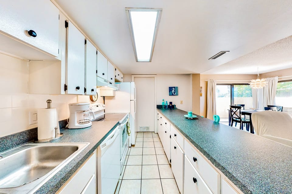 Clean and functional beach stay kitchen with ample counter space, full appliances, and coastal accents. Perfect for preparing meals and snacks before or after a day at the beach, with an open layout that flows into dining and living areas.
