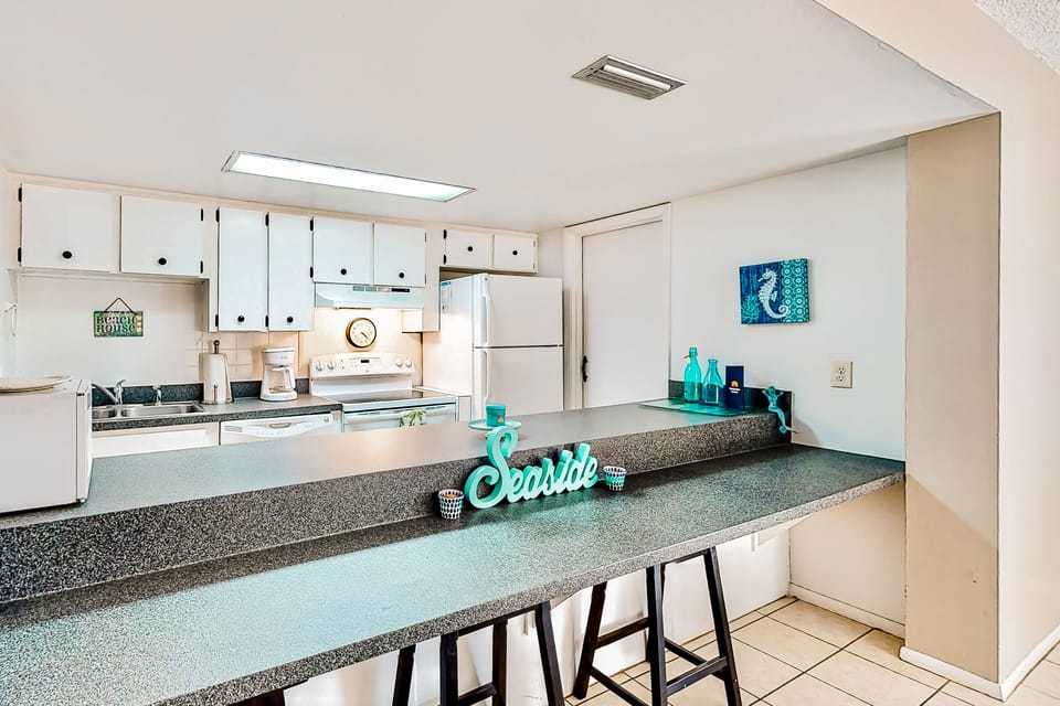 Inviting beach stay kitchen with a spacious breakfast bar, coastal décor, and full appliances. Perfect for casual meals, morning coffee, or gathering with family and friends before heading out for a day at the beach.