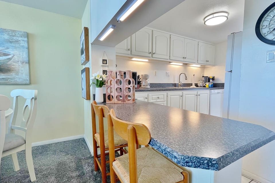 Enjoy casual meals in this open, beach-inspired kitchen featuring a spacious breakfast bar and full appliances—perfect for gathering after a day at the beach and relaxing during your comfortable beachfront vacation stay.