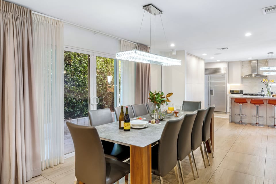 Formal dining room with a large rectangular table, modern chandelier, and large windows.