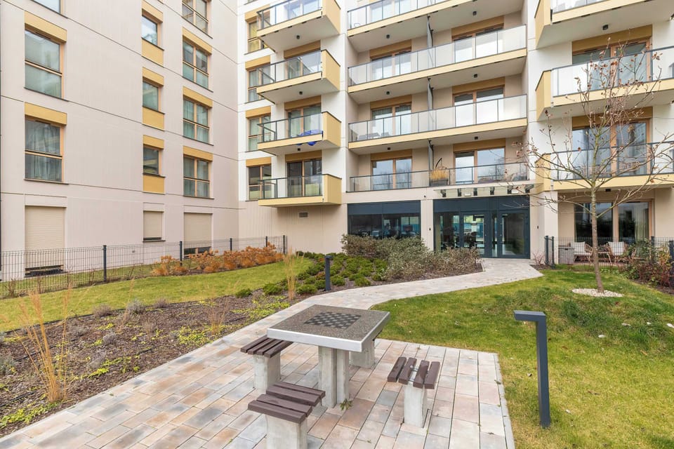 A slightly different angle of the landscaped yard with curved pathways and trees. Multiple balconies overlook the shared outdoor area. The mixture of grass and paving creates visual balance.