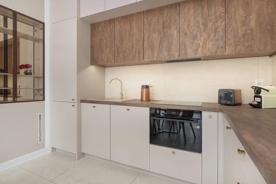 A modern kitchen with spacious countertops and streamlined wooden cabinets. Small appliances sit neatly arranged along the counter. The room feels functional yet stylish.
