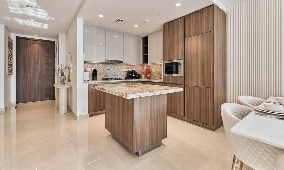 A sleek, fully equipped kitchen with marble countertops, wooden cabinetry, and modern appliances, including a stove, oven, microwave, Nespresso machine, toaster &amp; kettle, ideal for cooking and enjoying meals at home.