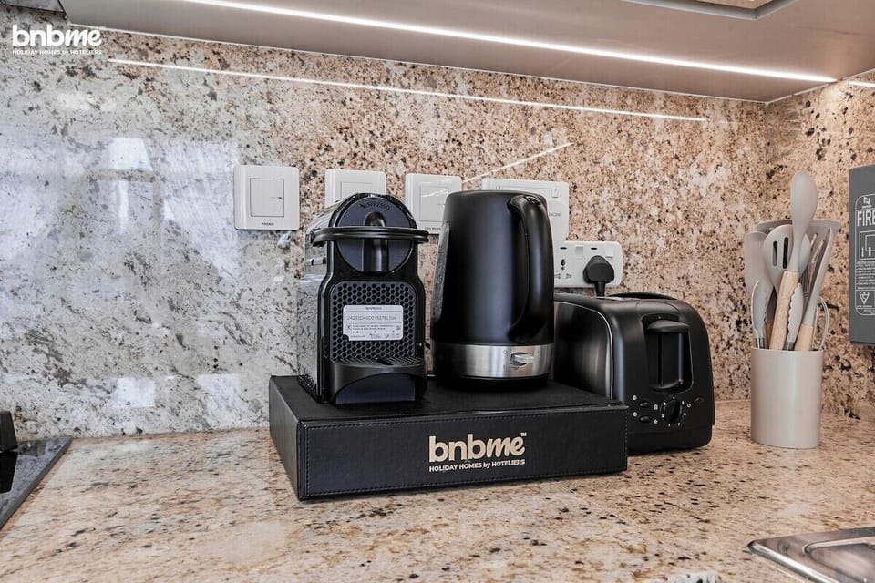 A sleek, fully equipped kitchen with marble countertops, wooden cabinetry, and modern appliances, including a stove, oven, microwave, Nespresso machine, toaster &amp; kettle, ideal for cooking and enjoying meals at home.